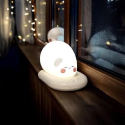 Lampa de veghe pisicuță iluminând noaptea, pe pervaz.